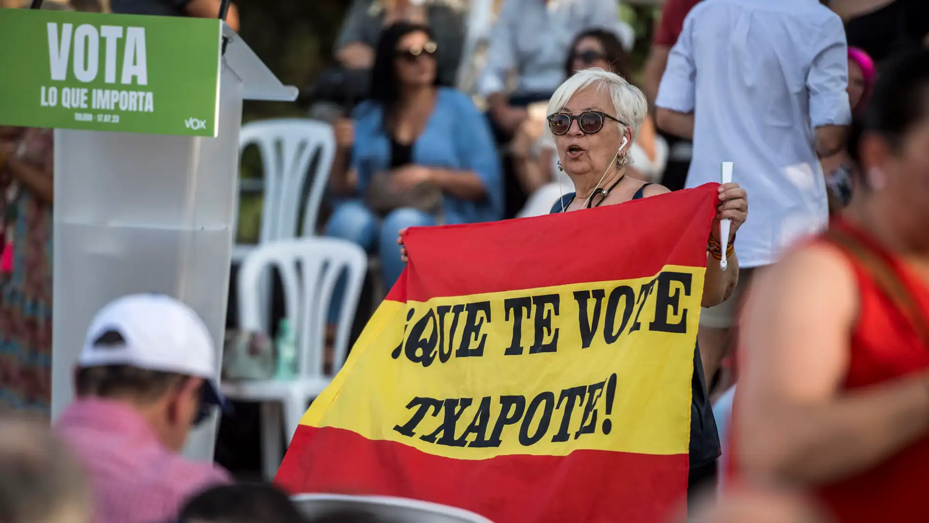 Una mujer esgrime una bandera con el lema "Que te vote Txapote" en un acto de VOX en Toledo