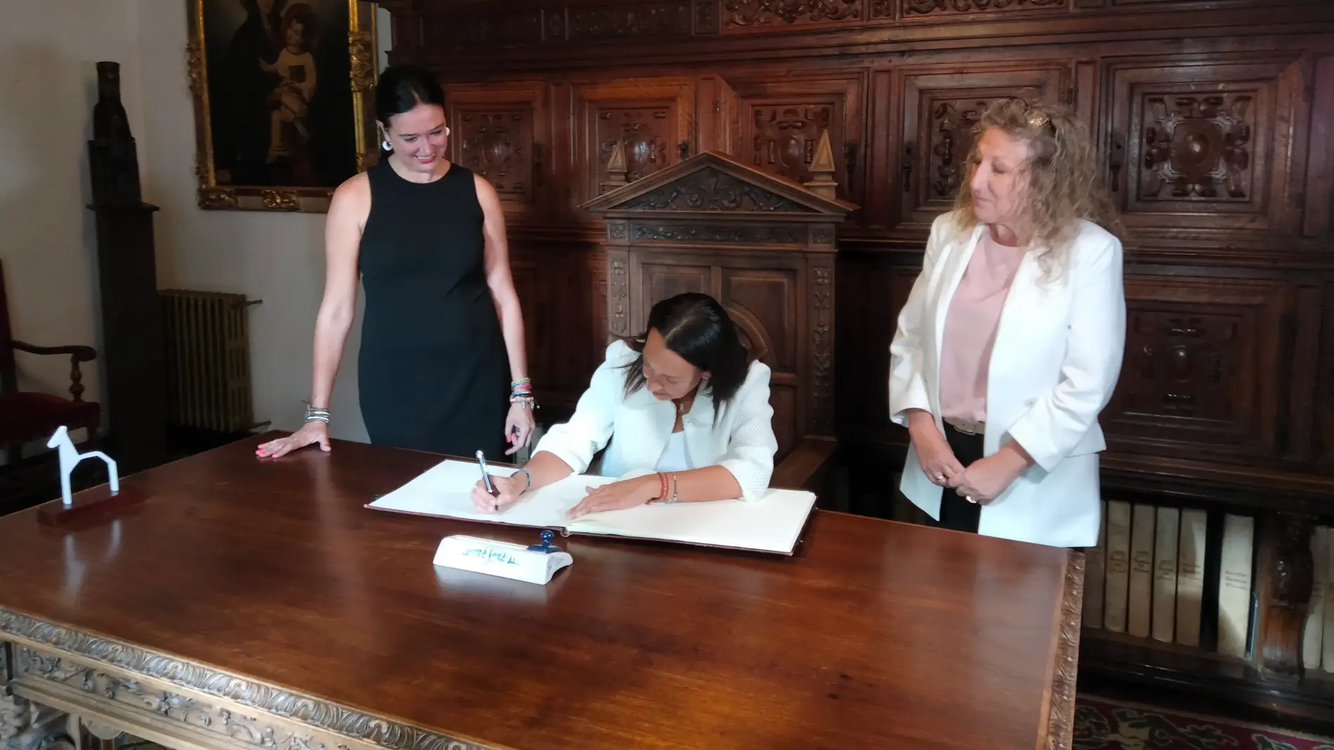 Carmen Susín firma el libro de visitas del Ayuntamiento ante la mirada de Lorena Orduna y Susana Oliván.