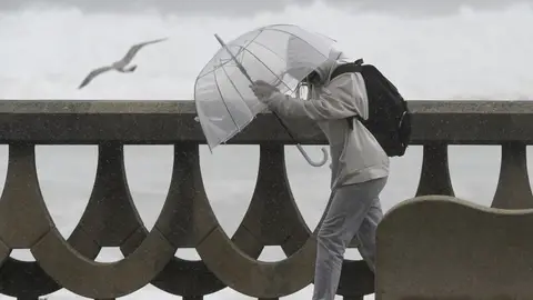 Una personas se protege de la lluvia y el viento con un paraguas Una personas se protege de la lluvia y el viento con un paraguas