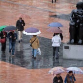 Viandantes con paraguas bajo la lluvia junto a La Maternidad de Botero. 