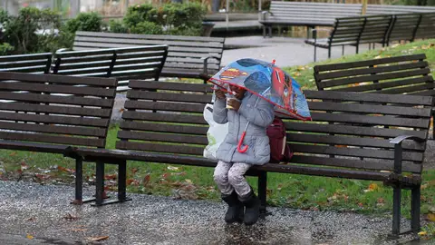 Una mujer come algo bajo la lluvia en Gijón Bajada drástica de temperaturas este domingo en casi todo el país