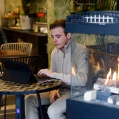  Un hombre utiliza un ordenador al lado de una chimenea en una cafetería este martes en Madrid