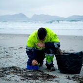 Un hombre recoge los pellets de plástico acumulados en la playa de Patos, en Nigrán, A Coruña.
