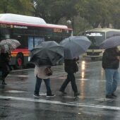 Imagen de varias personas bajo la lluvia en Sevilla durante el paso de la borrasca 'Karlotta'