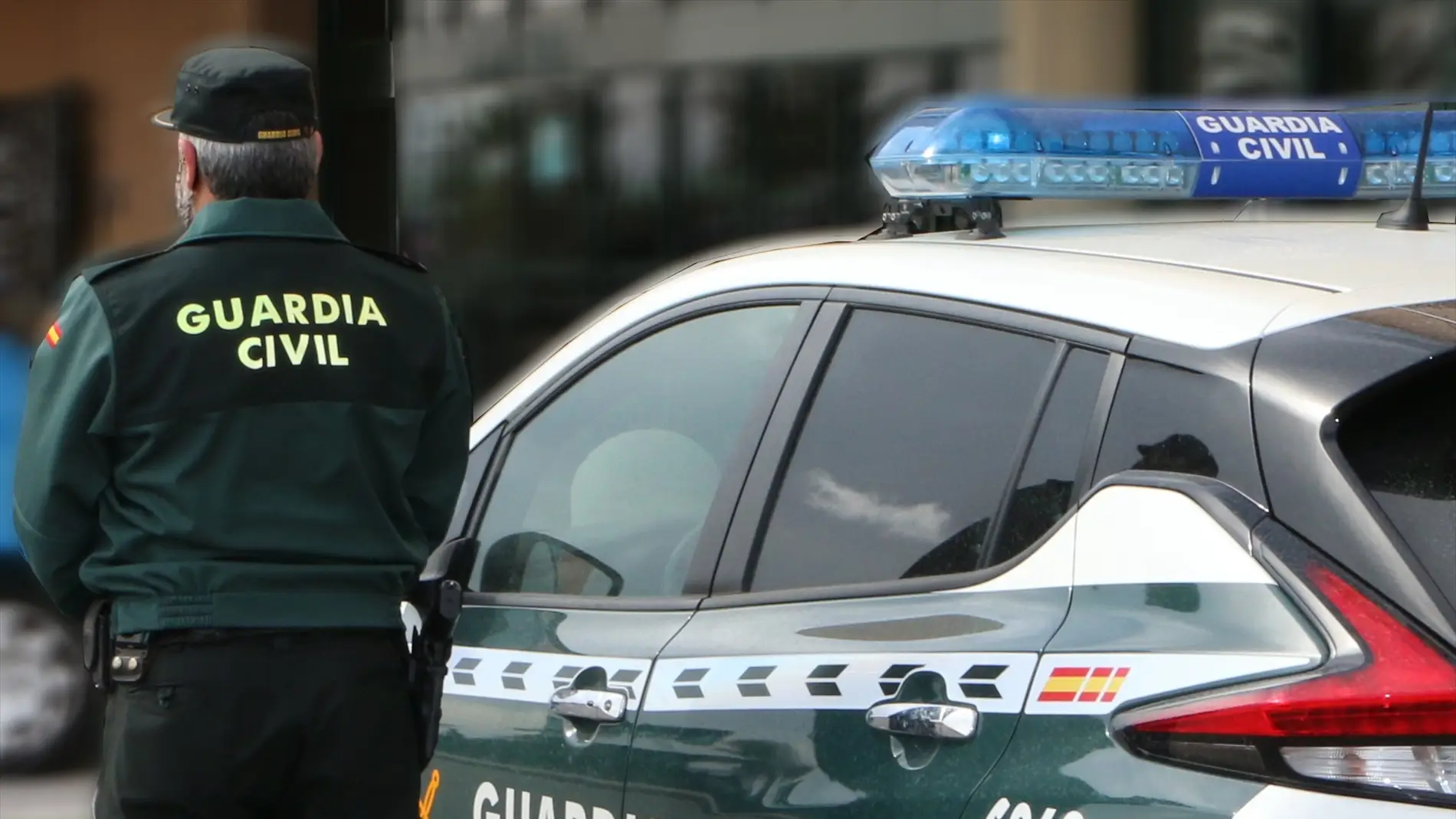 Un agente de la Guardia Civil, de espaldas, de pie junto a un vehículo oficial.