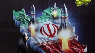 Una mujer iraní pasa junto a una pancarta antiisraelí con imágenes de misiles iraníes, en Teherán