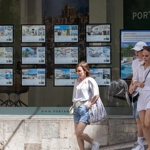 Varias personas pasan junto a los anuncios de viviendas en venta en una inmobiliaria