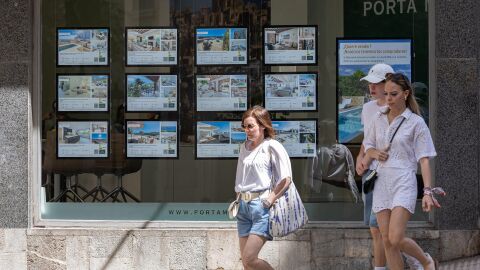 Varias personas pasan junto a los anuncios de viviendas en venta en una inmobiliaria