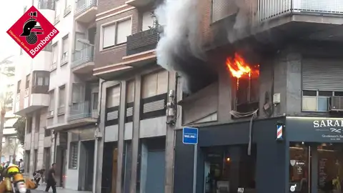 Las llamas salen por la ventana de la vivienda incendiada en Elche. Las llamas salen por la ventana de la vivienda incendiada en Elche.