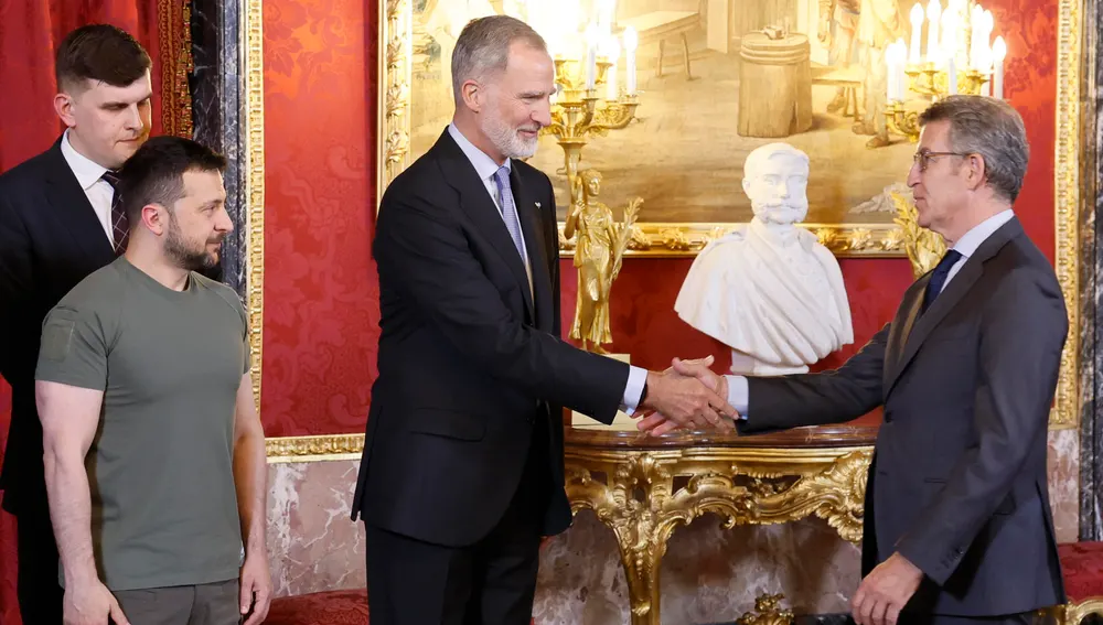 El rey Felipe VI, junto al presidente de Ucrania, Volodímir Zelenski (izda)​ saludan al líder del PP, Alberto Núñez Feijóo, a su llegada al almuerzo ofrecido en el Palacio Real, este lunes en Madrid. 
