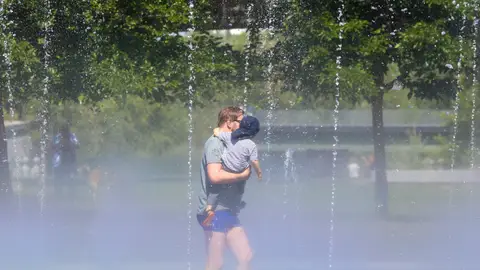 Un hombre con su hijo pasa por los chorros de agua de la playa de Madrid Río Un hombre con su hijo pasa por los chorros de agua de la playa de Madrid Río