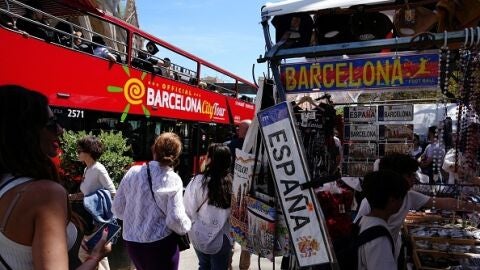 Varios turistas pasean junto a tiendas de souvenir y un autobús de visitas guiadas cerca de la basílica de Sagrada Familia en Barcelona.