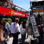 Varios turistas pasean junto a tiendas de souvenir y un autobús de visitas guiadas cerca de la basílica de Sagrada Familia en Barcelona.