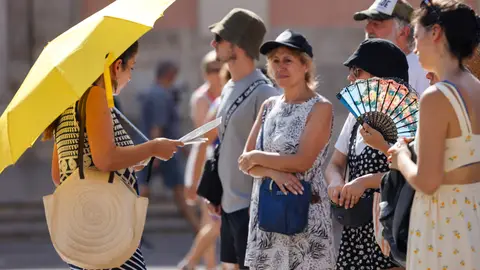 Un grupo de personas se protege del calor con parasol, abanico y gorras. Un grupo de personas se protege del calor con parasol, abanico y gorras.