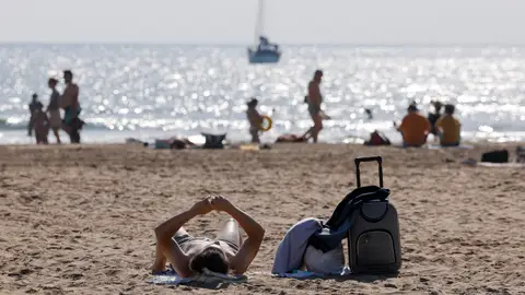 Imagen de archivo de un turista con su maleta tomando el sol en una playa valenciana este verano. Imagen de archivo de un turista con su maleta tomando el sol en una playa valenciana este verano.