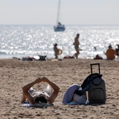 Imagen de archivo de un turista con su maleta tomando el sol en una playa valenciana este verano. Imagen de archivo de un turista con su maleta tomando el sol en una playa valenciana este verano.