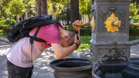 Una persona se refresca con agua de una fuente Una persona se refresca con agua de una fuente