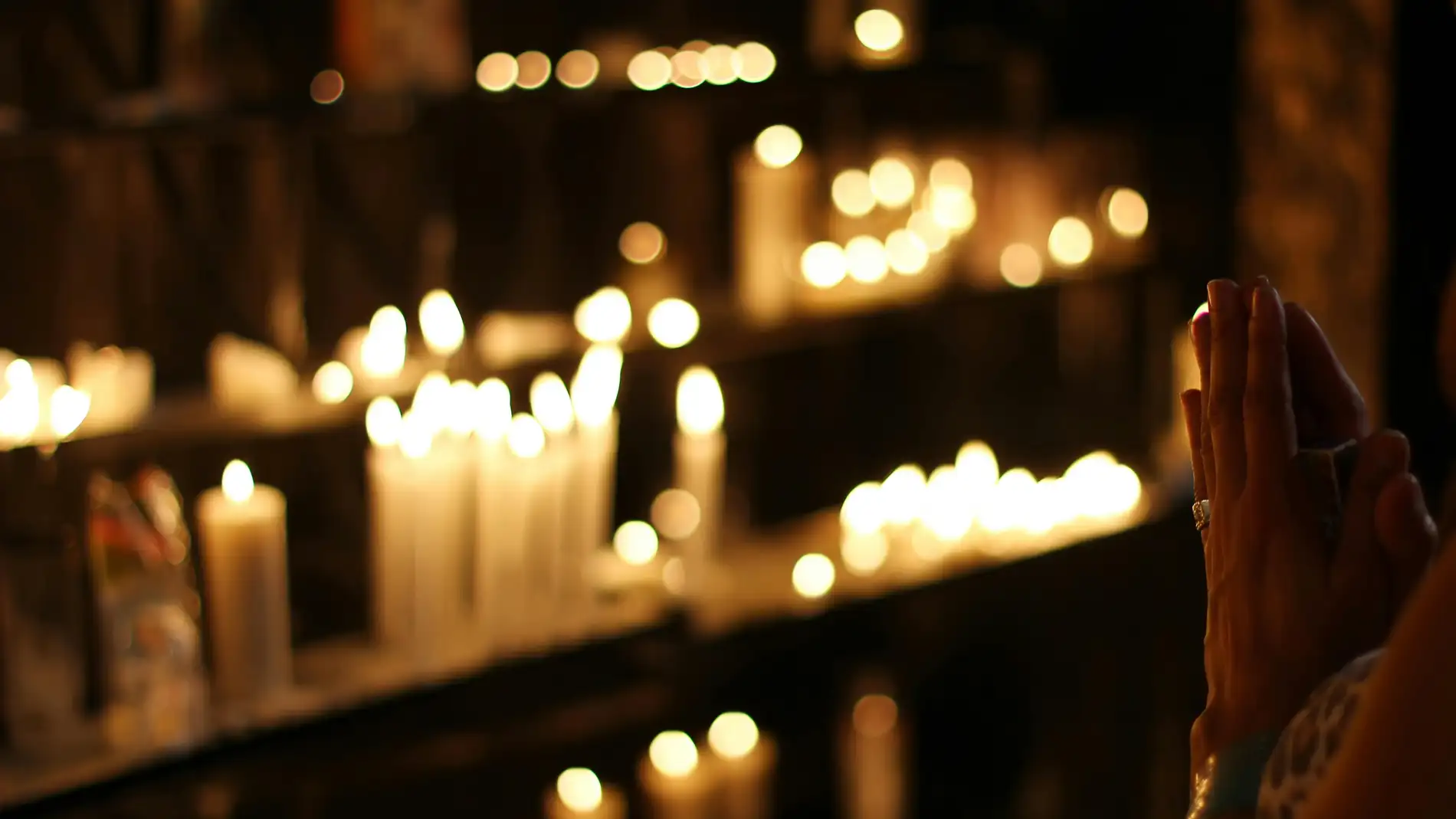 Manos juntas frente a unas velas Manos juntas frente a unas velas