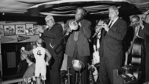 El trompetista y director de orquesta estadounidense Percy Humphrey toca junto a un trombonista y un clarinetista en el escenario detr&aacute;s de la barra del Paddock Lounge de Bourbon Street en Nueva Orleans.