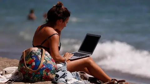 En la imagen de archivo, una mujer toma el sol mientras mira su ordenador portátil. EFE/ Jorge Zapata En la imagen de archivo, una mujer toma el sol mientras mira su ordenador portátil. EFE/ Jorge Zapata