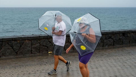 Dos personas pasean bajo la lluvia por el litoral de Arrecife, capital de la isla, durante una jornada de d&eacute;biles lluvias.