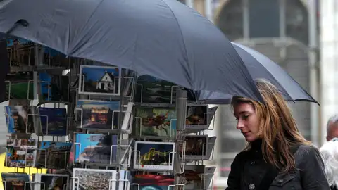 Una turista contempla unas postales protegidas por paraguas debido a la inestabilidad del tiempo. EFE/Kai Försterling/Archivo