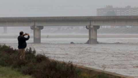 Una persona toma im&aacute;genes del nuevo cauce del Turia repleto de agua a causa de la gota fr&iacute;a que sufre la Comunitat Valenciana, la peor de este siglo XXI,