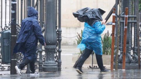 Dos personas caminan bajo la lluvia junto al Rectorado