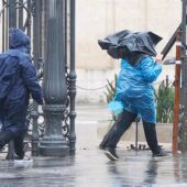 Dos personas caminan bajo la lluvia junto al Rectorado