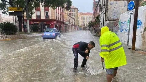 Varias personas intentan levantar la tapa de una alcantarilla en una calle inundada de agua debido a las fuertes lluvias en Málaga. Varias personas intentan levantar la tapa de una alcantarilla en una calle inundada de agua debido a las fuertes lluvias en Málaga.