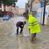 Varias personas intentan levantar la tapa de una alcantarilla en una calle inundada de agua debido a las fuertes lluvias en Málaga.