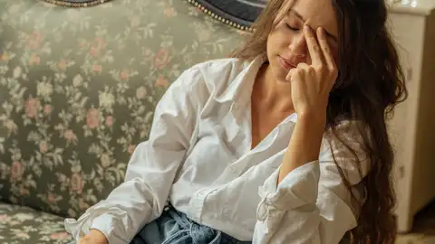Ocho frases que la gente infeliz dice sin darse cuenta, según la psicología Chica reclinada en sofá pensativa con ojos cerrados