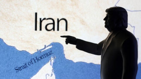 A map showing the Strait of Hormuz and Iran is seen behind a 3D printed miniature of U.S. President Donald Trump