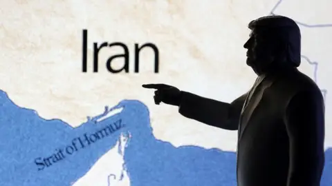 A map showing the Strait of Hormuz and Iran is seen behind a 3D printed miniature of U.S. President Donald Trump A map showing the Strait of Hormuz and Iran is seen behind a 3D printed miniature of U.S. President Donald Trump
