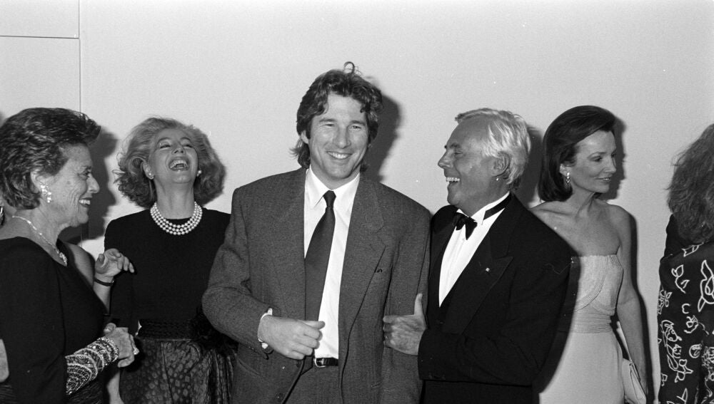 El actor Richard Gere muestra la etiqueta de su traje al diseñador Giorgio Armani, mientras los invitados observan el intercambio con la socialité Lee Radziwill.