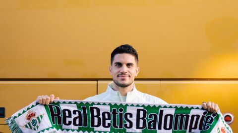 Marc Bartra posa con una bufanda del Betis antes del vuelo de la expedici&oacute;n verdiblanca a Lieja.