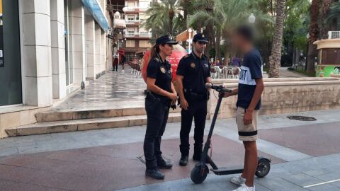 Dos agentes de la Polic&iacute;a Local junto a un usuario de patinete el&eacute;ctrico en el centro de Elche.