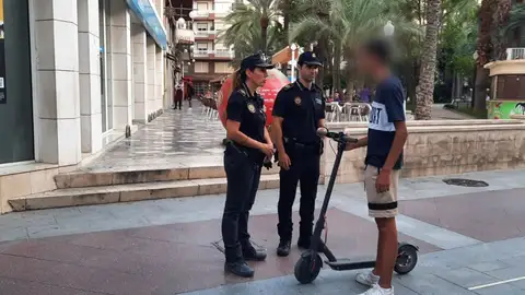 Dos agentes de la Policía Local junto a un usuario de patinete eléctrico en el centro de Elche. Dos agentes de la Policía Local junto a un usuario de patinete eléctrico en el centro de Elche.