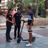 Dos agentes de la Policía Local junto a un usuario de patinete eléctrico en el centro de Elche.