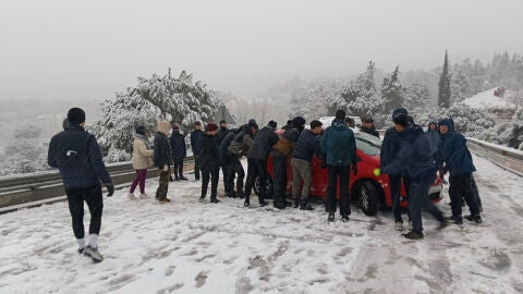 Varias personas tratan de mover un veh&iacute;culo atravesado en la carretera M-519 a la altura de Galapagar/ EFE/&Aacute;lvaro Blanco