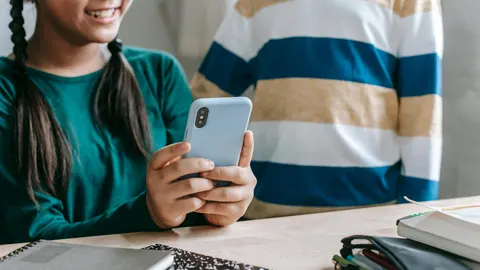 Unos niños utilizan el teléfono móvil.