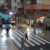 Ciudadanos con paraguas cruzando un paso de peatones en Elche. 