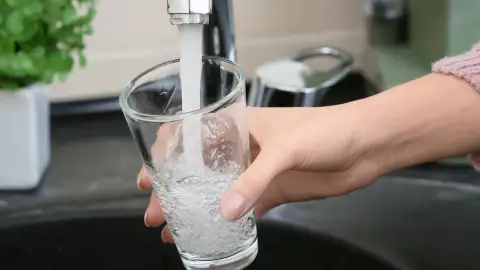 Un grifo de agua abierto con un vaso de agua Un grifo de agua abierto con un vaso de agua
