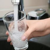 Un grifo de agua abierto con un vaso de agua