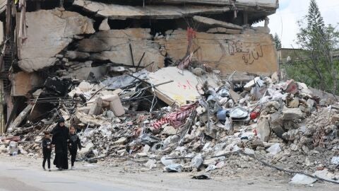 Personas caminan junto a los escombros de un edificio da&ntilde;ado por un ataque a&eacute;reo israel&iacute; en la aldea de Jibchit, al sur del L&iacute;bano, el 21 de abril de 2026. 