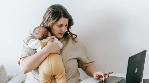 Imagen de archivo de una mujer trabajando con su bebé en brazos Imagen de archivo de una mujer trabajando con su bebé en brazos