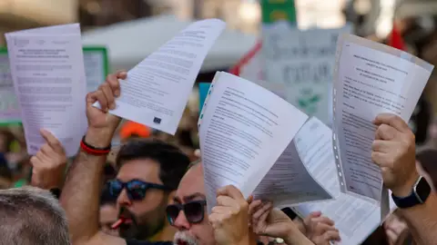 Miembros de equipos directivos de centros educativos de la Comunitat Valenciana muestran escritos de dimisión durante la concentración de profesores valencianos en las inmediaciones de Les Corts Valencianes este jueves. Miembros de equipos directivos de centros educativos de la Comunitat Valenciana muestran escritos de dimisión durante la concentración de profesores valencianos en las inmediaciones de Les Corts Valencianes este jueves.
