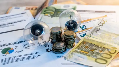 Dos bombillas sobre billetes, monedas y facturas, en una fotografía de archivo. Dos bombillas sobre billetes, monedas y facturas, en una fotografía de archivo.