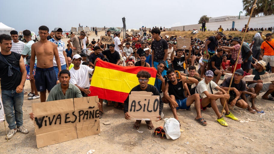 Un grupo de migrantes concentrados para solicitar asilo este domingo en la playa del trampol&iacute;n de Ceuta.
