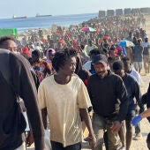 Un grupo de migrantes salen escoltados por la Policía de la playa de El Trampolín (Ceuta)